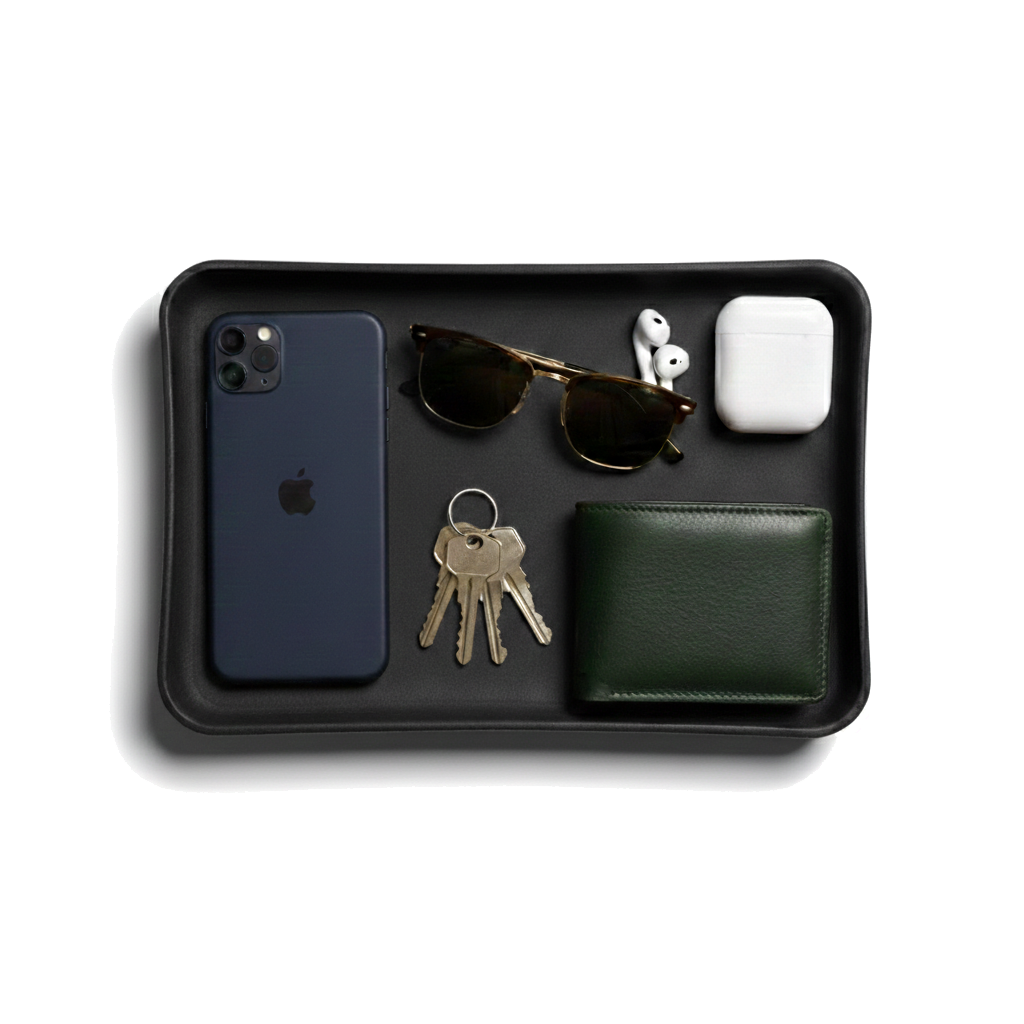 Black tray with phone, sunglasses, keys, wallet, and white device on a white background